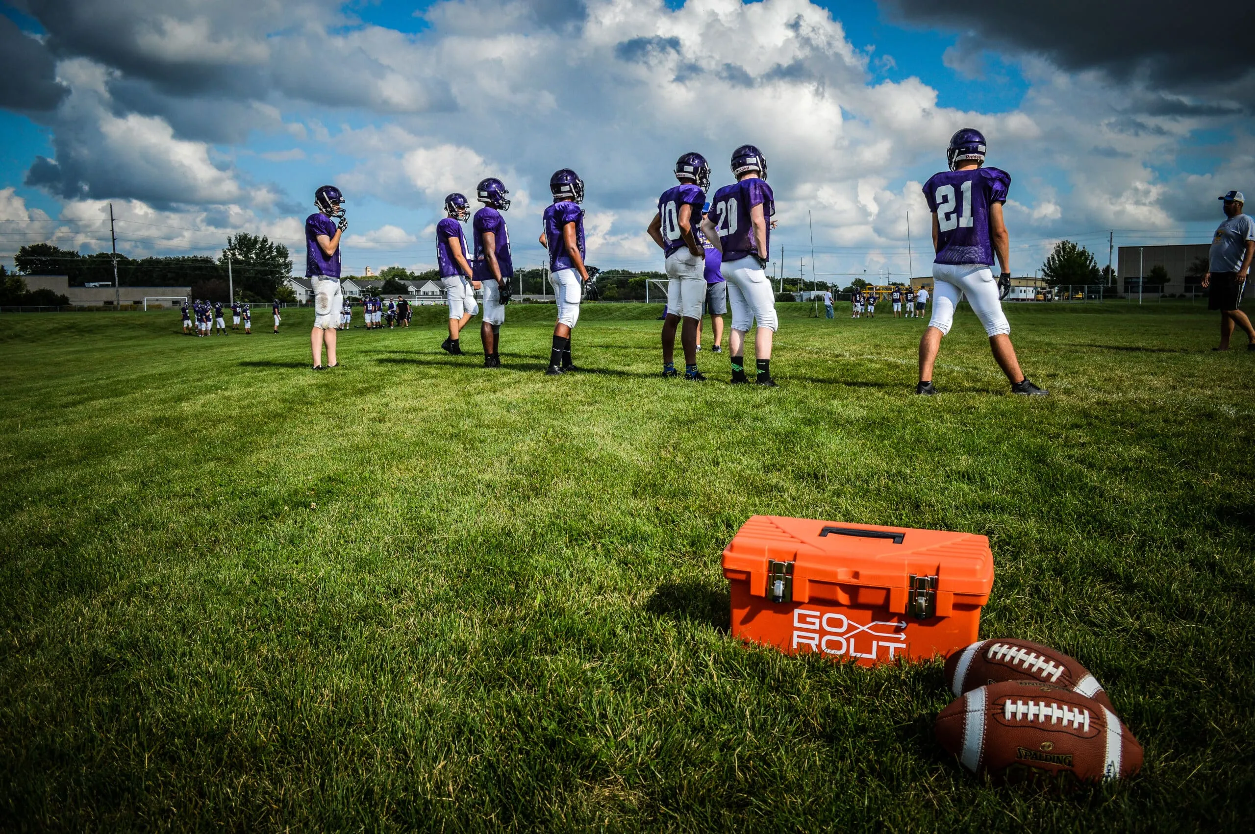 gorout branded carrying case and two footballs in front of football team practicing