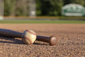 baseball against baseball bat laying on ground in infield