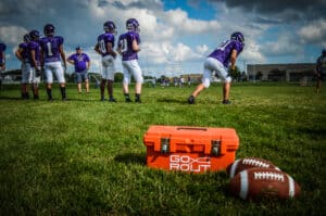 gorout orange device carrying case on practice field with two footballs next to it