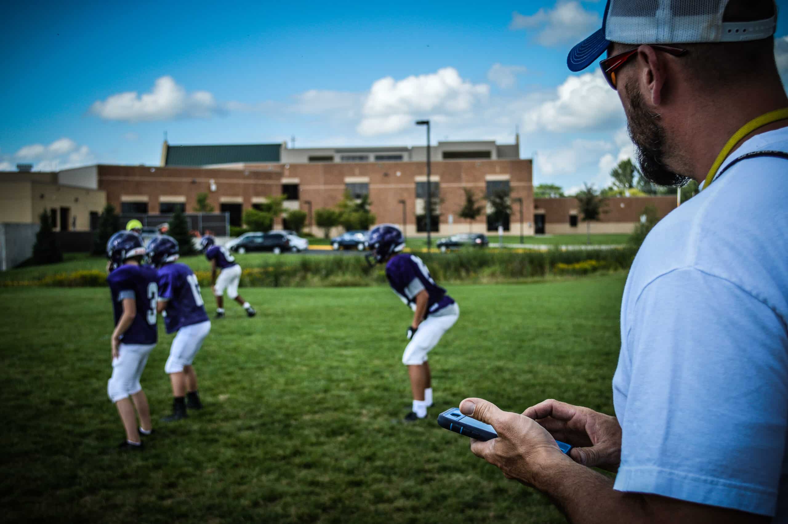 youth football coach watching practice with phone device