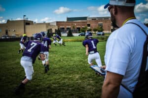 football coach watches players run at practice