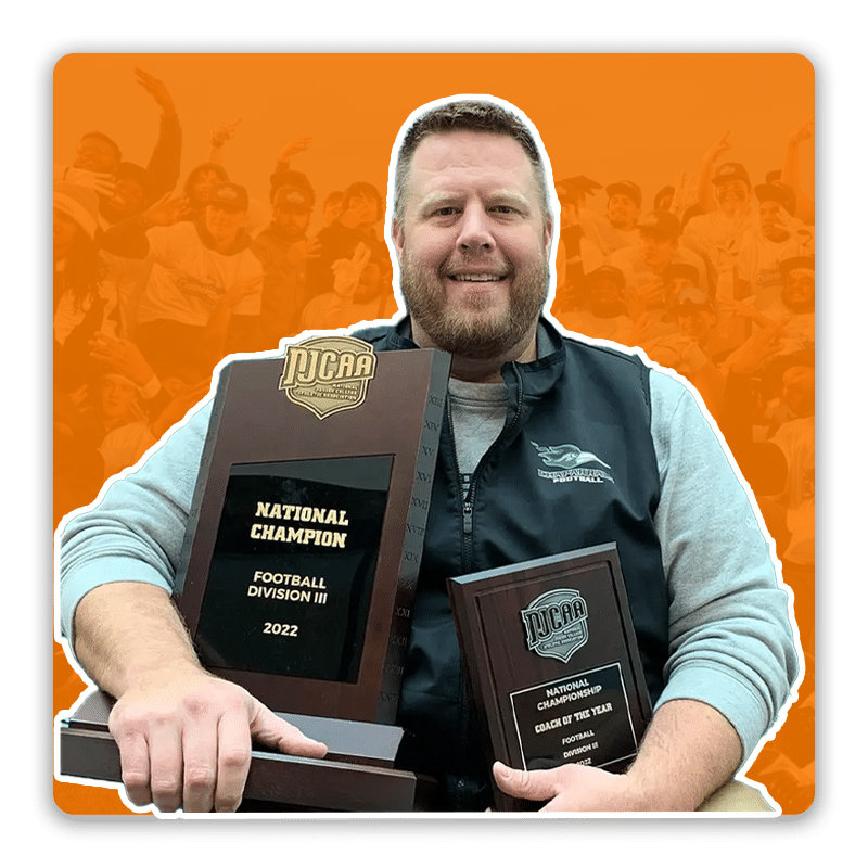 A high school football coach holding multiple championship trophies