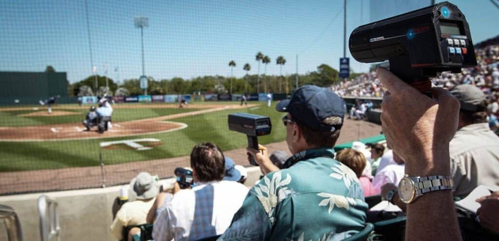 Baseball scouts look on from the bleachers recording pitch speeds with a radar gun