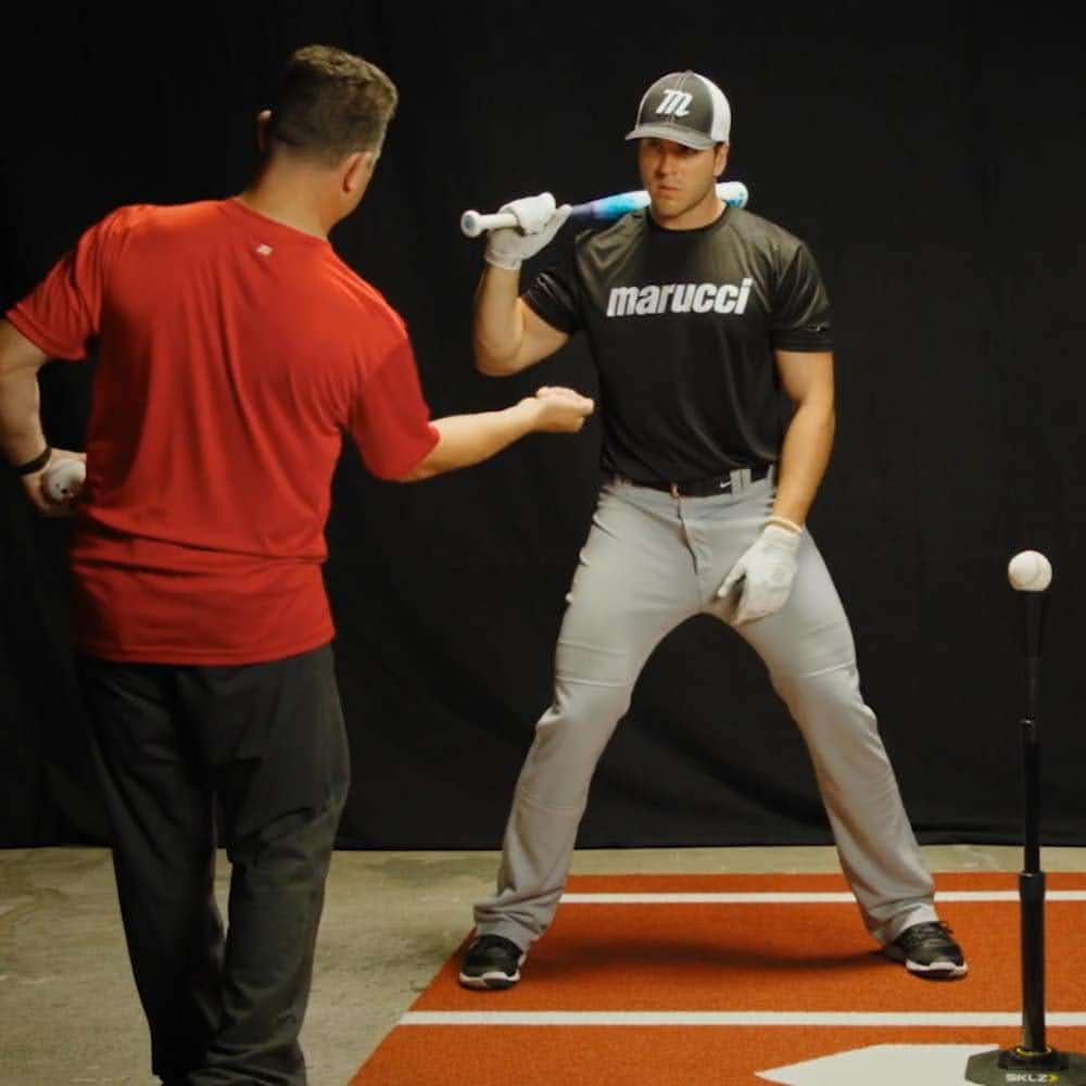 Baseball coach instructing player on bat path with tee drills