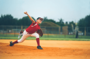 Youth baseball pitcher fully extends as he delivers a pitch to the plate