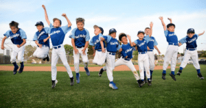 youth baseball team jumping in celebration in outfield grass