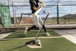 baseball player hitting ball on tee in batting cage