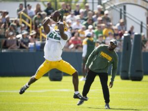 green bay packers player catching ball at practice while coach watches