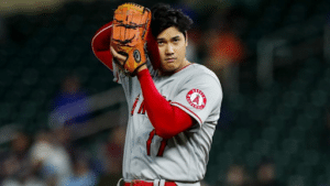 shohei ohtani holding hat with pitchcom device close to ear