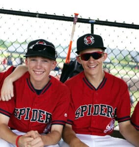 two travel baseball teammates smile for camera in dugout