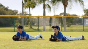 two youth baseball players laying on stomach in outfield grass