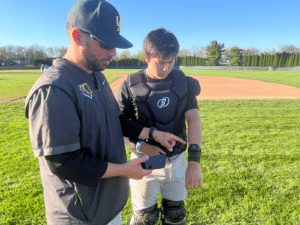 baseball coach instructing catcher on how to use gorout pitch calling device 