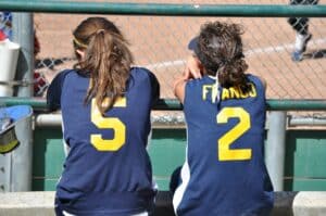 two softball players sitting together watching game