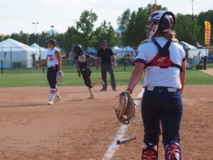 softball player rounds first base as catcher and first baseman watch